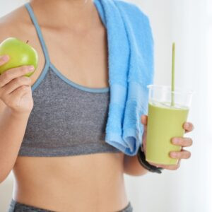 Crop Dot de femme méconnaissable dans des vêtements de sport tenant une pomme verte fraîche et un smoothie de désintoxication sur fond blanc