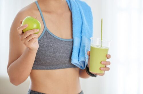 Crop Dot de femme méconnaissable dans des vêtements de sport tenant une pomme verte fraîche et un smoothie de désintoxication sur fond blanc