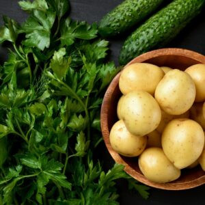 Pommes de terre crues fraîches dans un bol en bois, du persil vert et des concombres sur fond sombre, vue sur le dessus