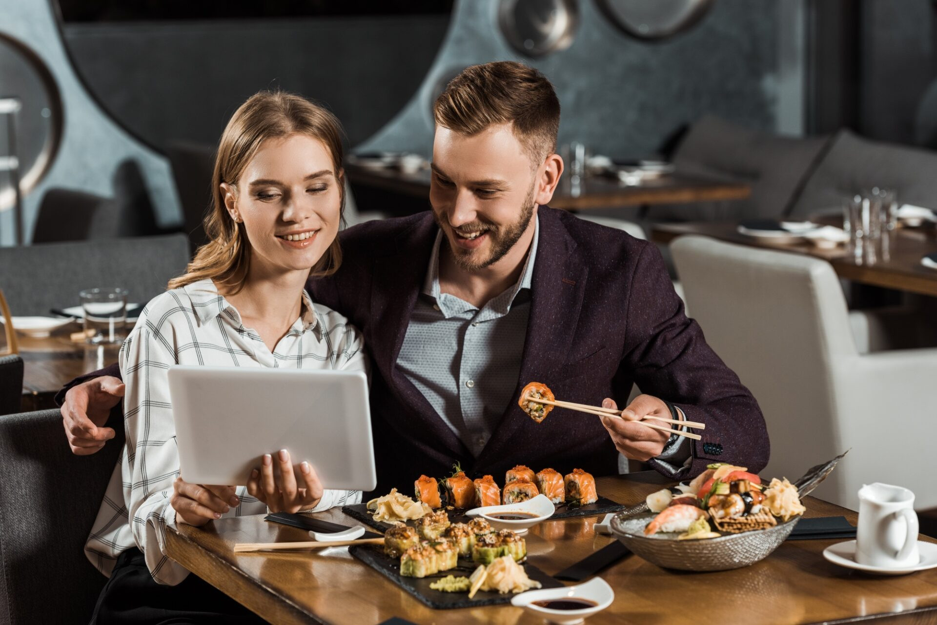 Couple attrayante de jeunes adultes utilisant une tablette numérique tout en mangeant des sushis dans le restaurant
