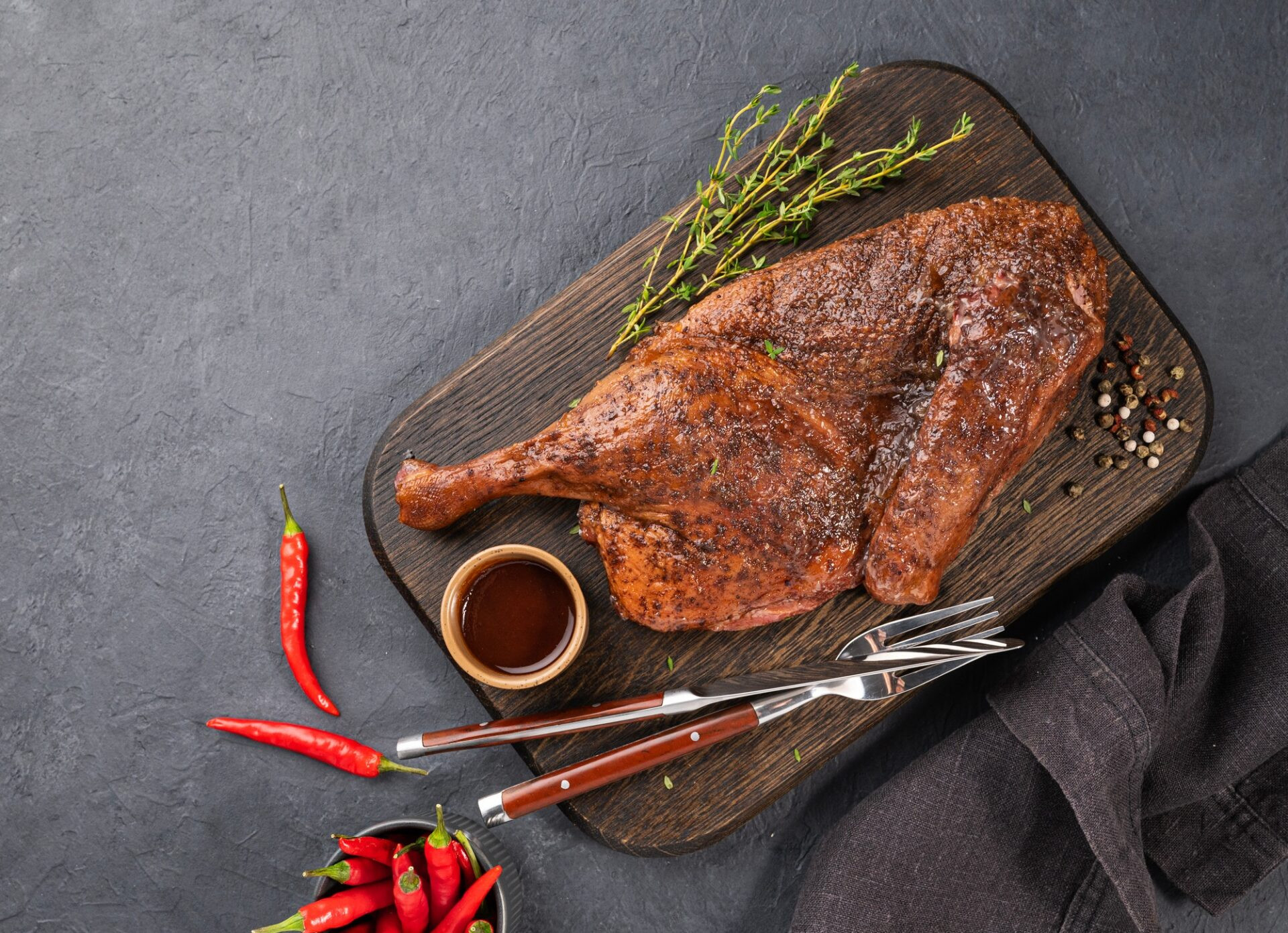 Duck rôti ou poulet rôti en épices et marinade sur une planche en bois avec des épices fraîches et du piment sur fond sombre. 
