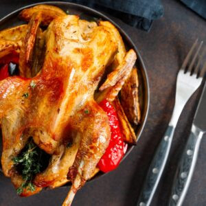 Volaille d'Inde rôtie avec des herbes et de l'huile d'olive sur un plat avec une garniture de pommes de terre et du poivron rouge.