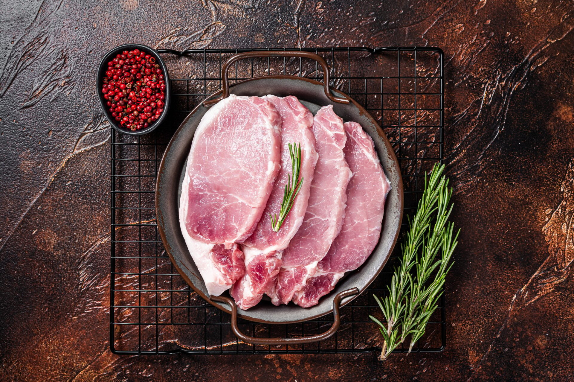 Steaks de coupe de porc cru dans un plateau en acier avec romarin. 