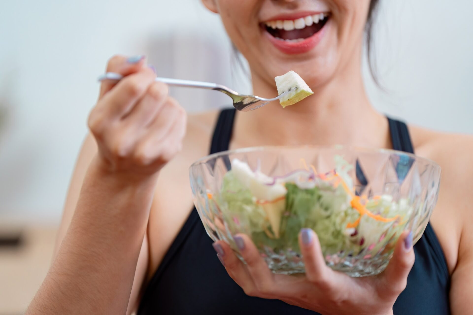 Un gros plan d'une jeune femme souriant tout en prenant une bouchée d'une salade colorée, mettant l'accent sur de saines habitudes alimentaires et l'importance de la nutrition pour le bien-être.